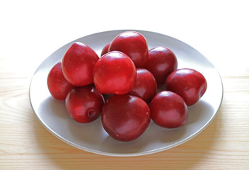 Fresh Gulf Ruby Plum Fruits Piled up on White Plate Served on Wooden Table 