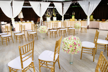Gold chiavari chairs setting for wedding venue decoration with big bouquet on the long glass vase on the aisle way