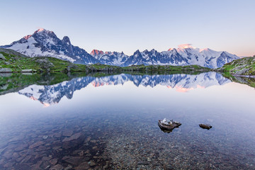 Snow covered mountain range reflected in a lake during morning moments before sunset. Amazing calm water. Cold feeling, beautiful view. Panorama. Stones in foreground. Hike, travel, trek, wander, fun.