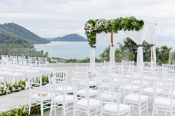 Wedding venue on the hill, white chiavari chairs, flowers, floral and green leafs decoration, ocean view background