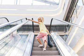 low angle view of smiling little child with shopping bag in hand on escalator at mall
