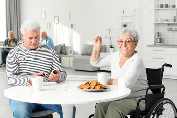 Senior woman playing dominoes with her friend while having breakfast at care home