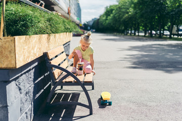 selective focus of little child eating dessert while sitting on bench near skateboard at street