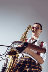 Obraz na płótnie Canvas low angle view of stylish young performer in sunglasses playing saxophone on grey