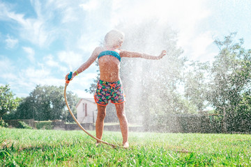 Cute little girl refresh herself from garden watering hose