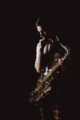 pensive young musician holding saxophone isolated on black