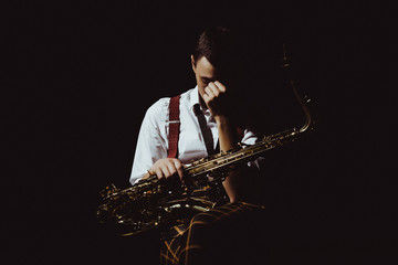Naklejka premium young musician holding saxophone isolated on black