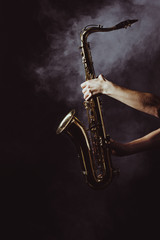 Fototapeta premium cropped shot of musician holding saxophone in smoke on black