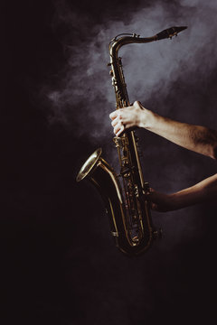 cropped shot of musician holding saxophone in smoke on black