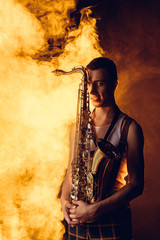 Fototapeta na wymiar handsome stylish young musician holding saxophone and looking at camera in smoke