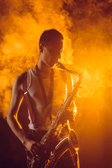 Fototapeta na wymiar handsome young musician playing saxophone in smoke