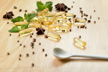 Fototapeta na wymiar Medicine herb, Cod liver oil omega 3 gel capsules with healthy medicinal plant on wooden brown tone background with a white spoon on foreground.