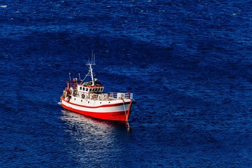 Aerial view of red fishing boat on a deep blue sea in Greece.