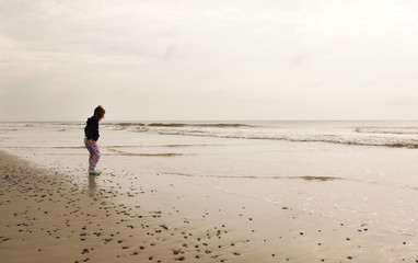 North Sea beach in Denmark at cloudy day. Small girl collecting stones.