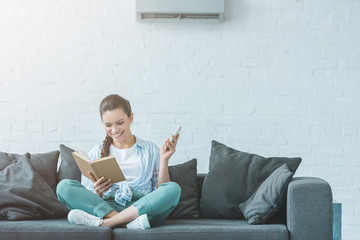 woman reading book while turning on air conditioner with remote control