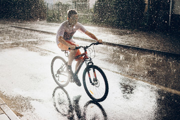 young boy riding bicycle in rainy street in sunshine, summer moments. space for text. atmospheric moment. cycling and activity. stylish hipster having fun under rain