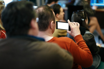 stylish man holding phone with empty white screen in audience and recording, sitting at meeting, business marketing lecture