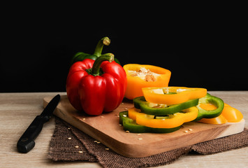 Colourful red,yellow and green peppers are placed on a wooden tray ready for cooking with black background,Bell pepper slice,Selective focus