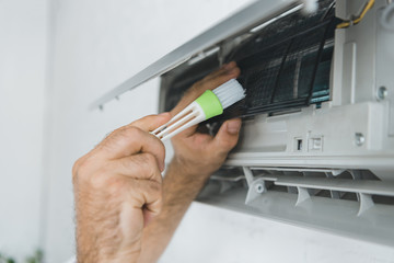 cropped view of male worker cleaning air conditioner with brush