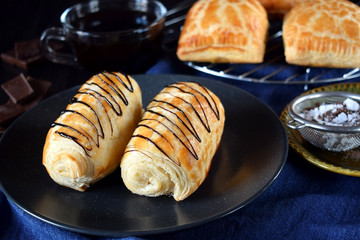 Two golden buns decorated with chocolate on a dark plate