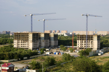 Three buildings, three construction cranes against the background of the sky.