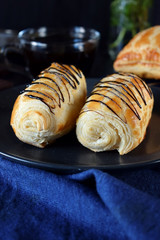 Two golden buns decorated with chocolate on a dark plate