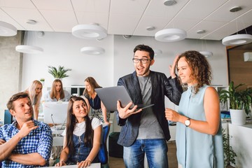 Successful company with happy employees in everyday clothes brainstorm while standing with a laptop in a modern office
