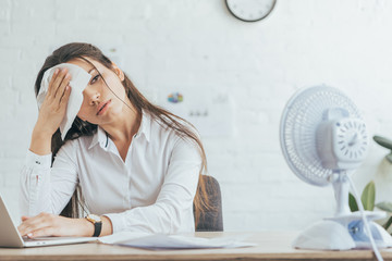 sweaty businesswoman working in office with electric fan