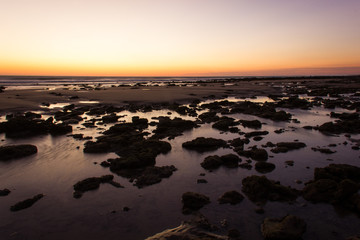 Rocks over shallow water on low tide with lovely sunset on the background in Zahora Beach, South Spain. Fabulous twilight by the sea, peaceful dusk concepts