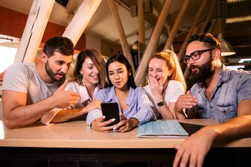 Friends sitting at the bar at the table looking at the phone screen