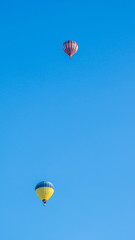 Two multi color hot air balloons flying into blue sky