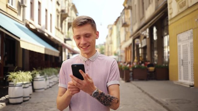 Smiling handsoman man walk on street use phone happy smartphone summer sun tourist adult business hipster caucasian cell office messaging slow motion portrait outdoor sms close up old city
