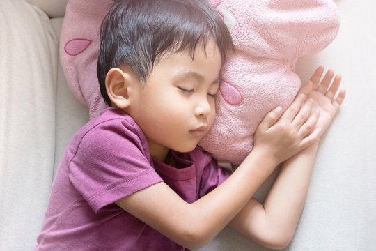 Cute little asian boy sleeping in bed at home. Pink purple tone color image.