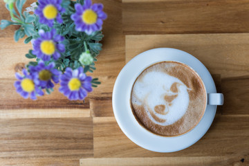 Latte art coffee cup with purple flowers vase on wooden table, top view