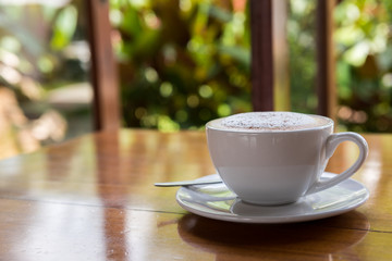 Cappuccino cup on wooden table with bokeh of trees