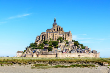 Fototapeta na wymiar General view of the Mont Saint-Michel tidal island, located in France on the limit between Normandy and Brittany, from the bay at low tide under a summer blue sky with salt meadow in the foreground.