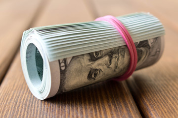 A pack of twisted 100 dollar bills . On a wooden table. Close up
