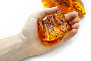 Beautiful pieces of amber one on a white background another in the hand. A luminous piece of amber in the palm of your hand. Sun stone. Petrified resin natural crystal material for jewelry. Vintage