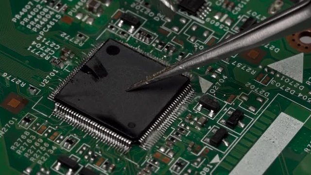 Desolder of surface-mounted electronic chip microprocessor using the soldering iron from the circuit board. Reflowing contacts of electronic microprocessor. Closeup macro.