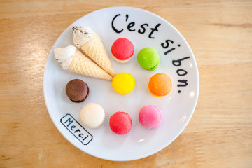 Mix color of macaroon on wihte plate with french language put on soft wooden table from top