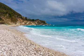 Fototapeta na wymiar Pebble beach, stormy blue sea, green hill and gray sky in Dominican Republic