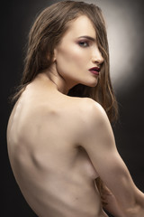 Fototapeta premium Beautiful slim flexible athletic topless girl model covers her naked breast with her hair on grey black gradient background. Healthy skin. Copy space.