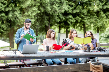 Young friends dressed casually studying with colorful books sitting at the table outdoors in the park