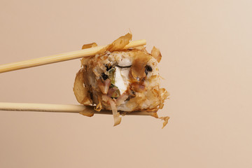 A Bonito roll with some cream cheese, a salmon and some smoked tuna shavings. close up of chopsticks taking portion of sushi roll on light background / eating sushi roll using chopsticks.