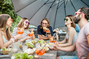 Young friends having fun together with snacks and drinks during the evening light outdoors in the park cafe