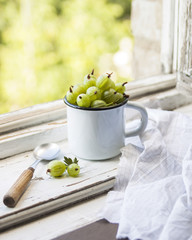 Summer berries in a white cup with green gooseberry on a white background. Gooseberry green, fresh ripe berries, healthy food concept. Detox life. Copy space