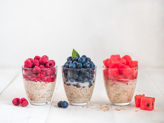 Healthy breakfast: overnight oats with fresh fruits and berries in glass. Overnight oatmeal porridge with watermelon, raspberry, blueberry,decorated mint. Overnight oats on white background,copy space