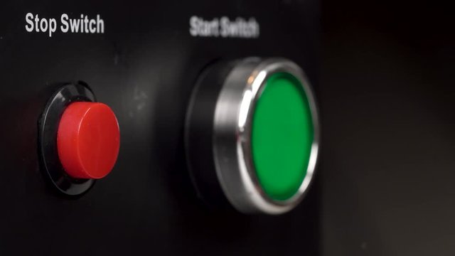 Closeup of two buttons in the frame. Green start switch and red stop switch buttons. Finger press the red stop switch button.