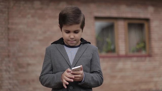 Handsome little Boy use his phone. Background of bick wall