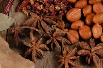 Collection of asian cooking spices on wooden plank including peanuts star anise pepper corns ginger and dry chili peppers